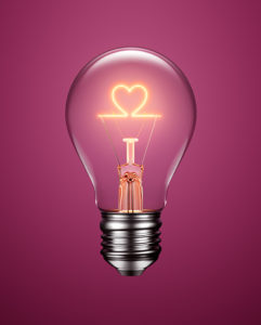 Light bulb with filament forming a heart icon on purple background