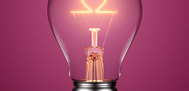 Light Bulb With Filament Forming A Heart Icon On Purple Background