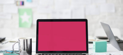 A Photograph Of A Laptop On A Desk That Has A Pink Screen And A Coffee Cup