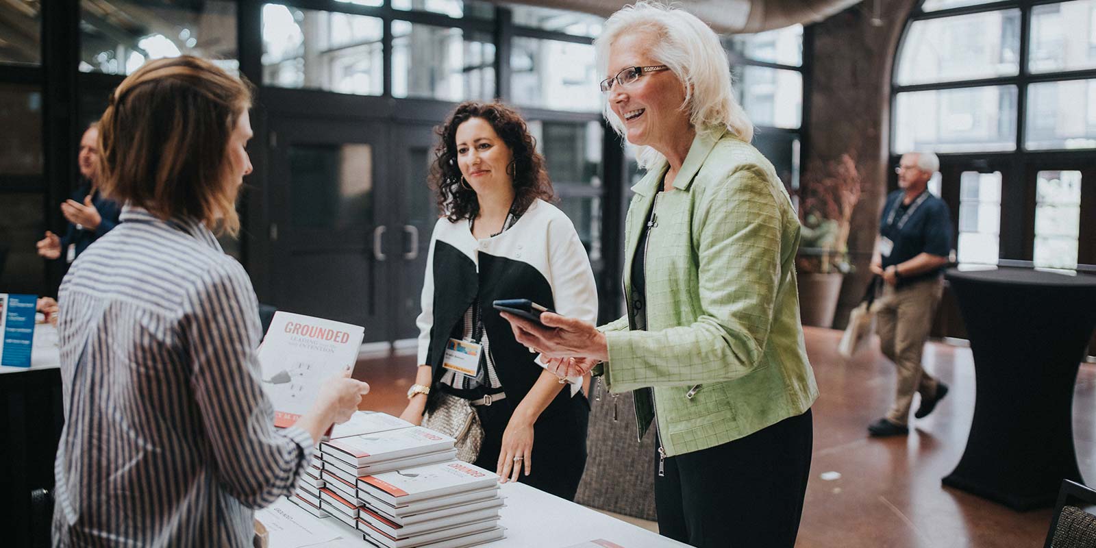 A photograph of Nancy M. Dahl talking with people who are buying her book