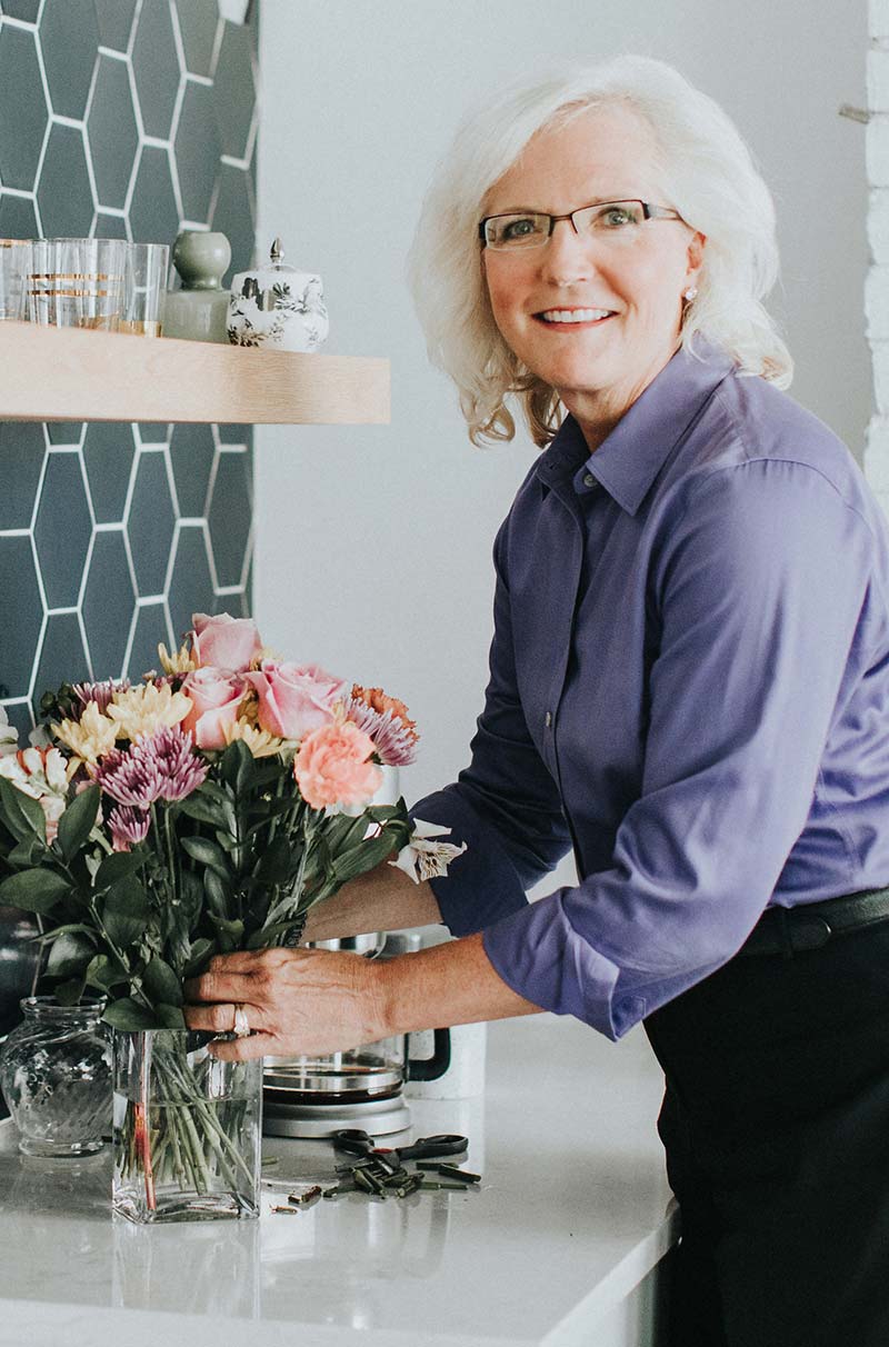 Photograph of Nancy M. Dahl wearing a purple shirt putting flowers into a vase
